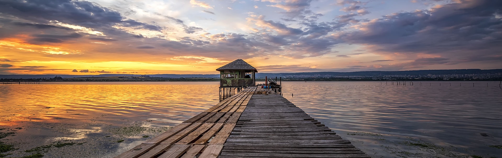 Exciting colorful long exposure landscape on a lake with a wooden pier and small house in the end.