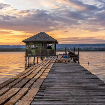 Exciting colorful long exposure landscape on a lake with a wooden pier and small house in the end.