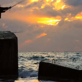 Fisherman on pier at sunset